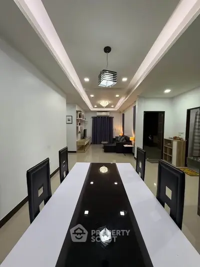 Modern dining area with sleek black and white table, leading to a cozy living room.