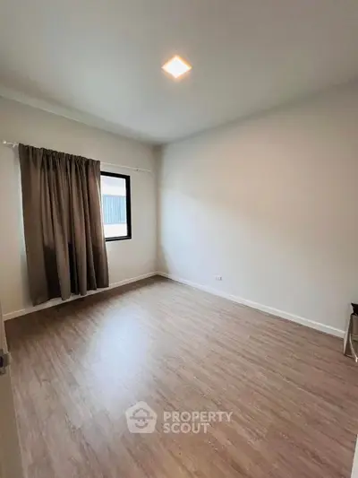 Spacious empty room with wooden flooring and large window, perfect for customization.