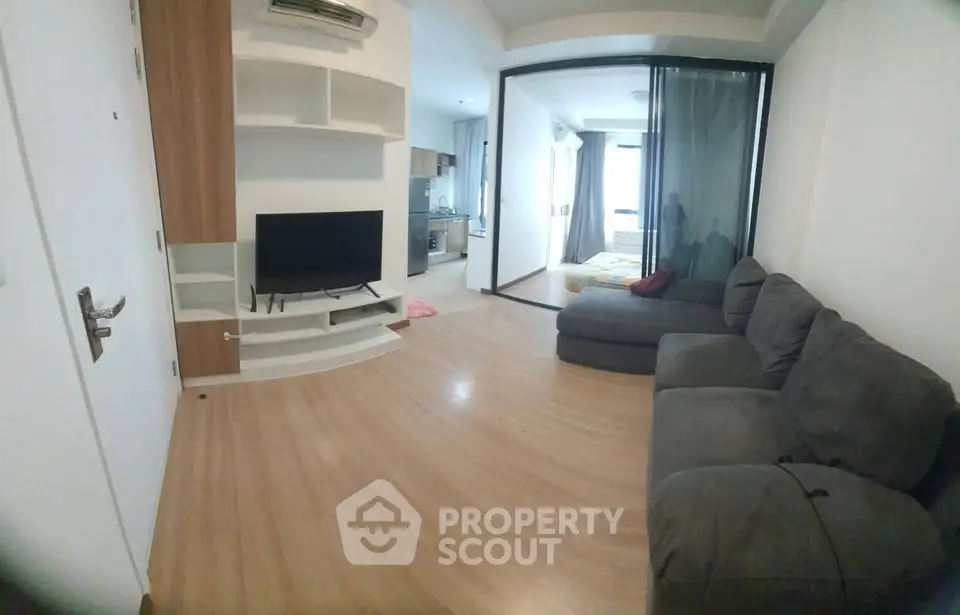 Modern living room with cozy sofa and TV, open layout leading to kitchen and bedroom.