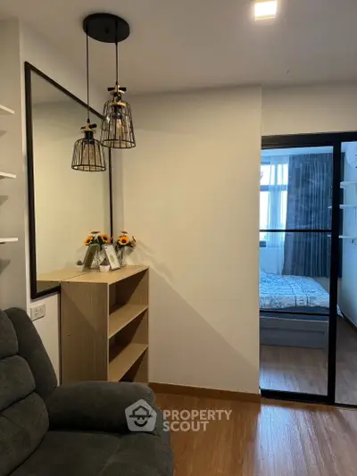 Modern apartment interior with cozy living room and view into bedroom, featuring stylish lighting and wooden flooring.