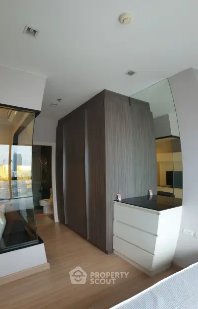Modern bedroom with sleek wooden wardrobe and mirrored dresser, offering a glimpse into a stylish bathroom.
