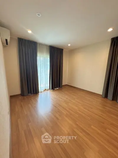 Spacious empty room with wooden flooring and large window with curtains