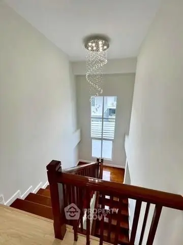 Elegant staircase with modern chandelier and wooden railing in a bright home interior.