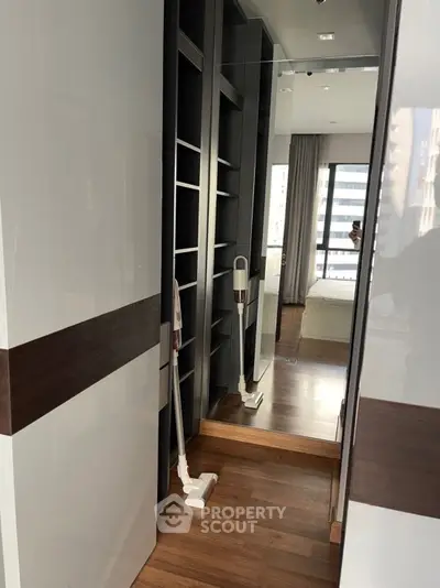 Modern bedroom with sleek wooden flooring and built-in shelving, featuring a large window with city view.