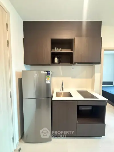 Modern compact kitchen with sleek cabinetry and stainless steel fridge in a stylish apartment.