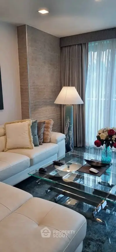 Elegant living room with modern white sofa and glass coffee table, featuring stylish decor and natural light.