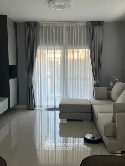 Modern living room with sleek furniture and large window draped with elegant curtains.