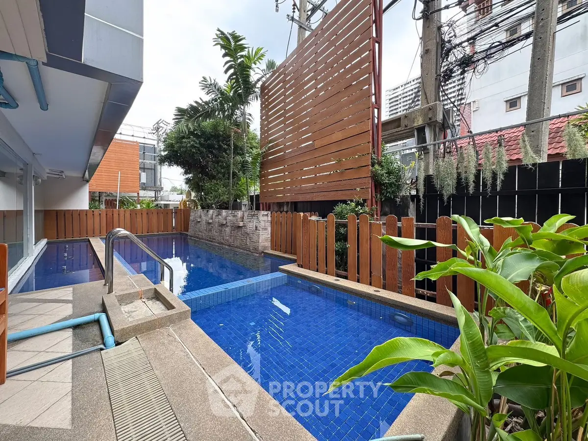Modern outdoor pool area with wooden fencing and lush greenery in urban setting.