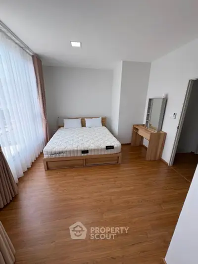 Spacious bedroom with wooden flooring and large windows for natural light