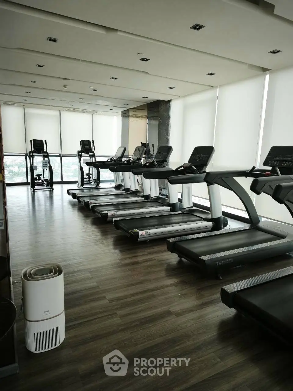 Modern gym with multiple treadmills and large windows offering city views.