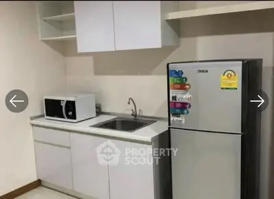 Modern kitchen with sleek cabinets, microwave, and stainless steel fridge.
