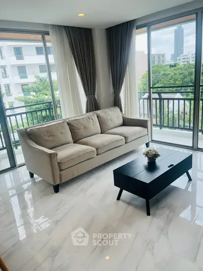 Spacious living room with modern sofa and coffee table, featuring large windows and city view.