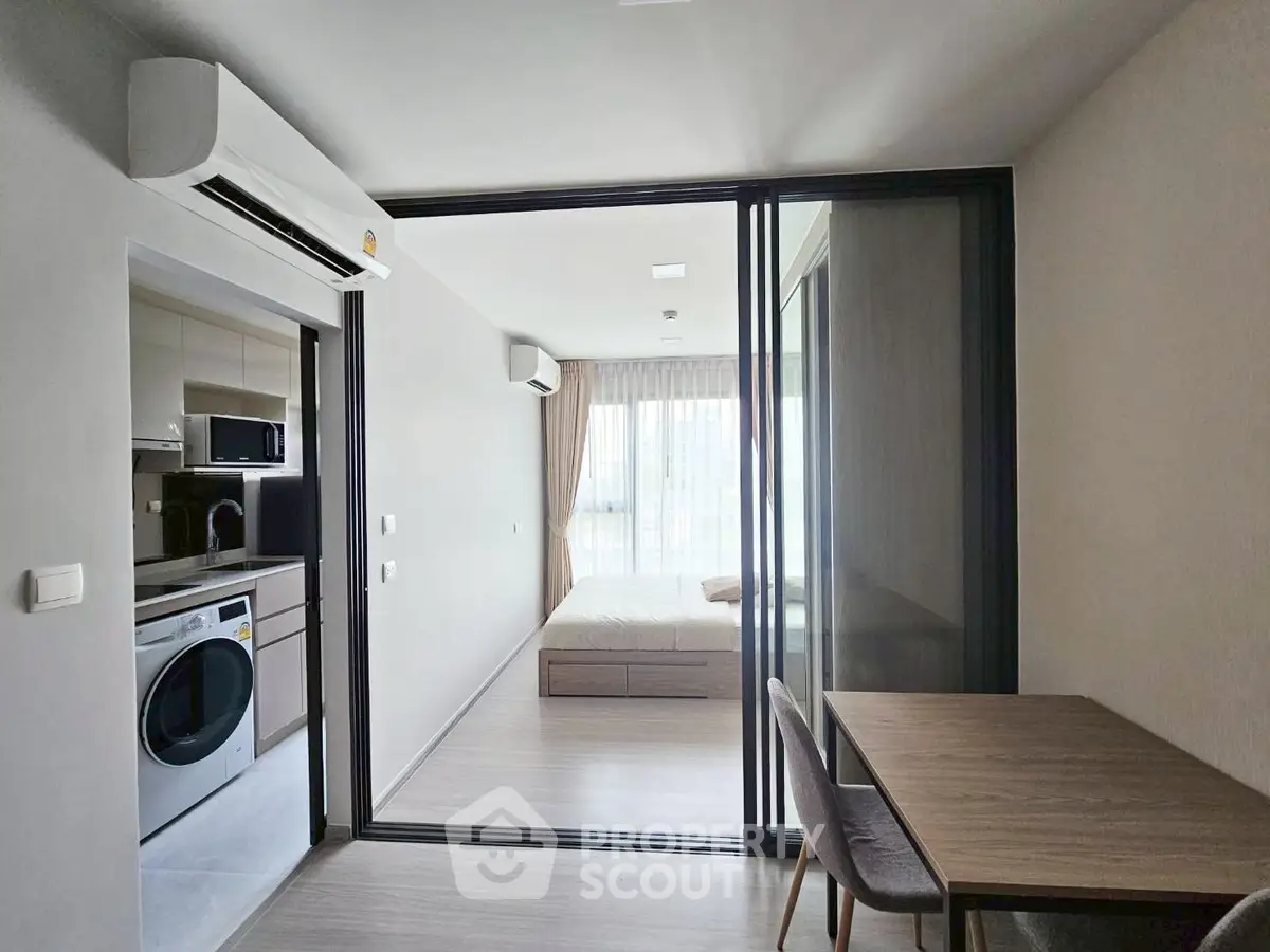 Modern apartment with open layout, featuring a cozy bedroom and compact kitchen with washing machine.