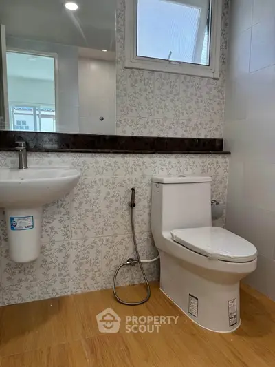 Modern bathroom with floral tiles and wooden flooring, featuring a sleek toilet and sink.