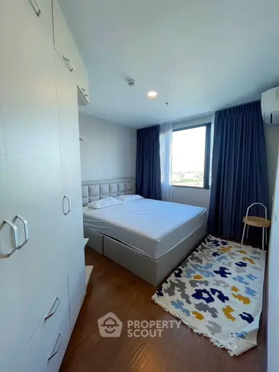 Cozy bedroom with modern decor and large window offering natural light and scenic view.