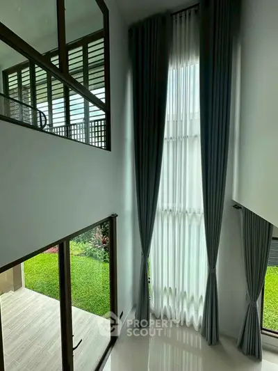 Elegant modern living room with high ceilings and large windows overlooking a lush garden.