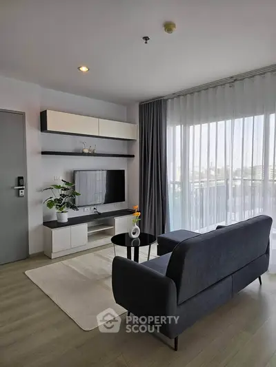 Modern living room with sleek furniture and large window offering natural light.