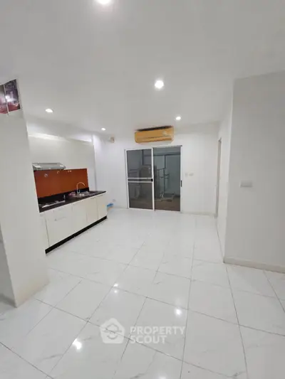 Modern kitchen with sleek white cabinets and open layout, featuring air conditioning and sliding glass door.