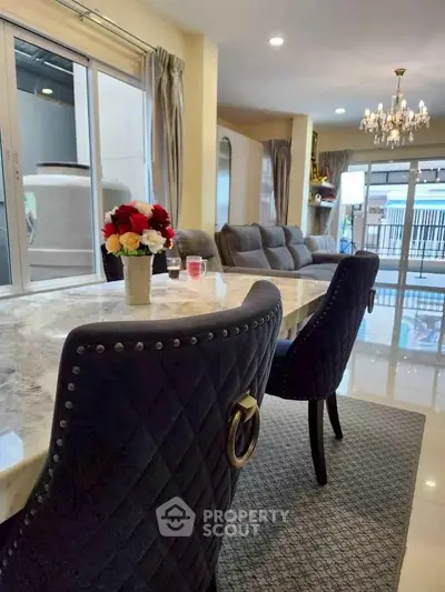 Luxurious living room with elegant dining area and plush seating, featuring a chandelier and large windows.