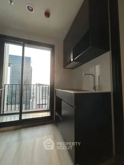 Modern kitchen with sleek black cabinetry and city view from balcony.