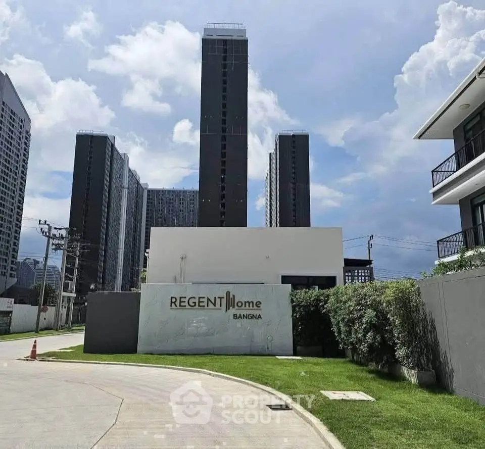 Modern high-rise residential building with lush green surroundings and clear blue sky.