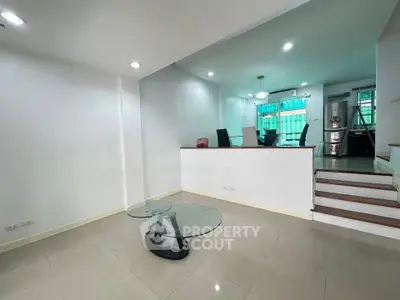 Spacious modern living room with glass coffee table and dining area, featuring sleek design and ample natural light.