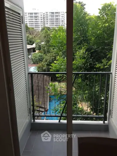 Charming balcony view with lush greenery and distant building, perfect for relaxation.