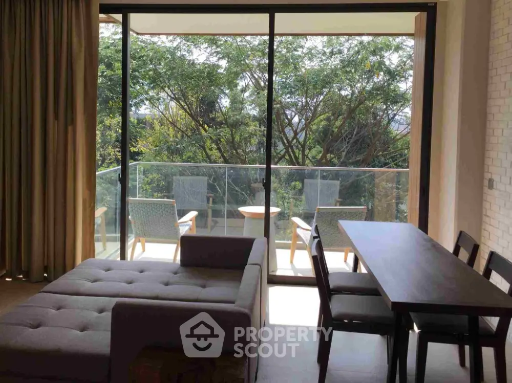 Spacious living room with large windows opening to a serene balcony view, modern furniture, and elegant dining area.