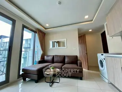 Modern living room with brown sectional sofa and washing machine, featuring large windows and balcony access.