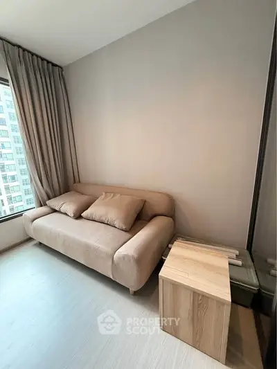 Modern living room with cozy beige sofa and wooden side table, featuring large window with city view.
