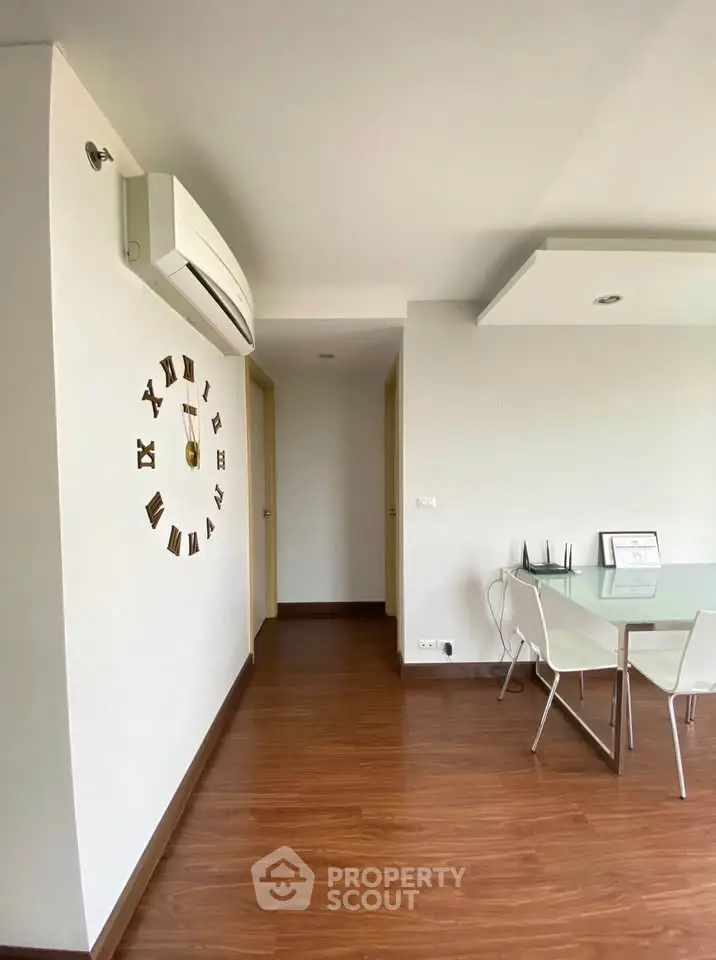 Modern living room with wooden flooring and stylish wall clock, featuring a sleek glass dining table and chairs.