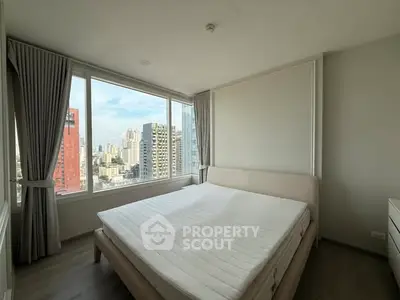 Spacious bedroom with city view and modern furnishings in high-rise apartment.