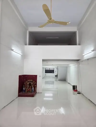 Spacious open-plan interior with high ceiling and glossy tiled floor, featuring a ceiling fan and decorative alcove.
