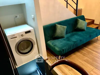 Stylish interior with modern washing machine and elegant teal sofa in cozy living space.