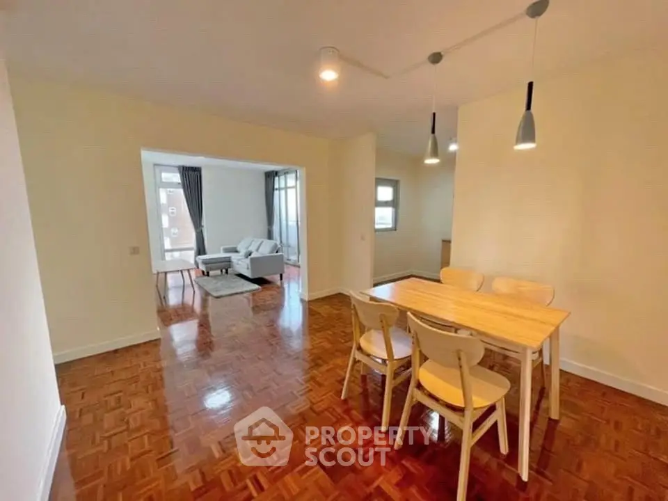 Spacious dining area with wooden flooring and modern lighting in open-plan apartment.