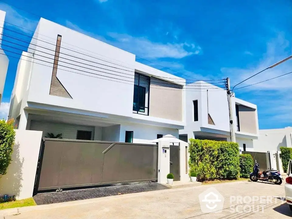 Modern white minimalist house with sleek design and large driveway under clear blue sky.