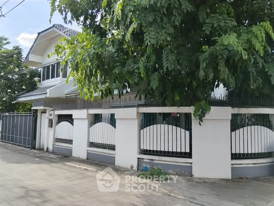 Charming two-story house with lush greenery and gated entrance in a serene neighborhood.