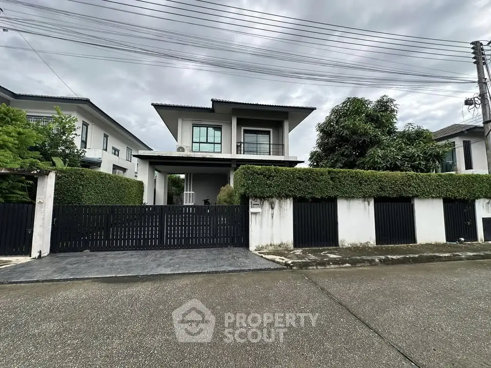 Modern two-story house with gated entrance and lush greenery in a suburban neighborhood.
