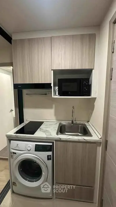 Compact modern kitchen with washing machine and microwave in a stylish apartment.