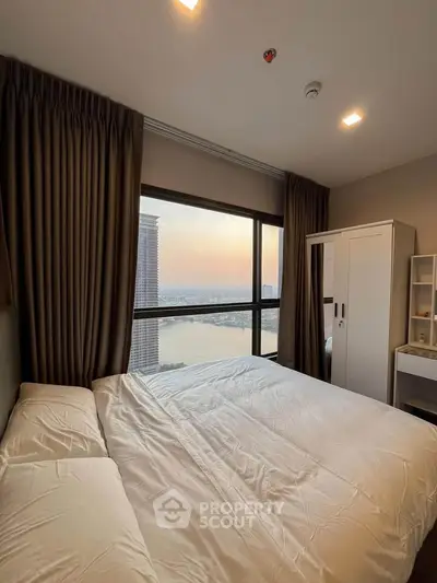 Cozy bedroom with stunning city and river view, featuring a large window and modern furnishings.