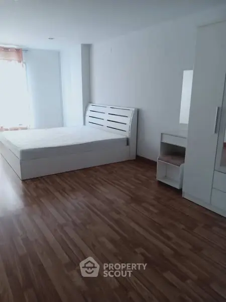 Spacious bedroom with wooden flooring and modern white furniture