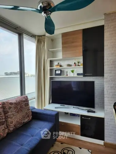 Cozy waterfront living room with modern furnishings, large windows offering natural light and serene views, complemented by a stylish ceiling fan.