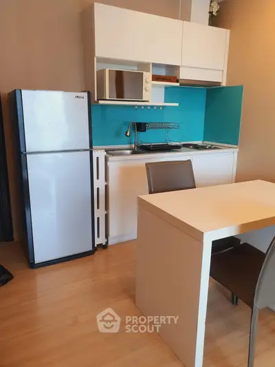 Modern compact kitchen with fridge, microwave, and dining table in cozy apartment.