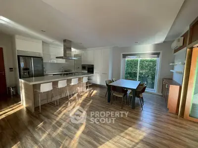 Modern kitchen with open layout and dining area, featuring sleek appliances and wooden flooring.