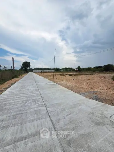 Expansive land plot with newly paved road under a vast sky, ideal for development opportunities.