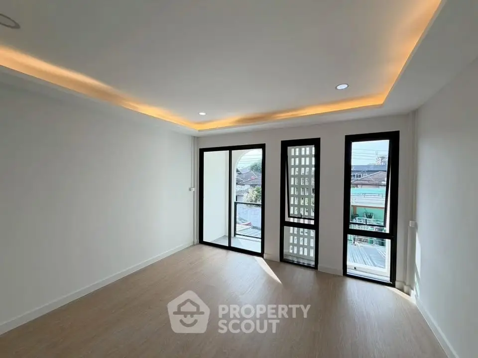 Spacious modern living room with large windows and balcony access, featuring elegant recessed lighting.