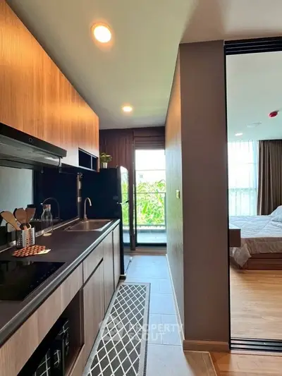 Modern apartment kitchen with sleek cabinetry and open layout leading to a cozy bedroom.