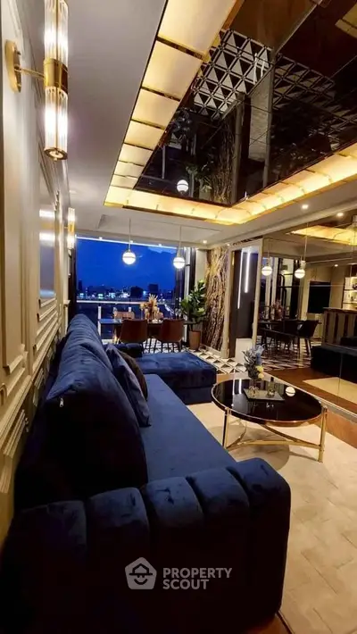 Luxurious living room with elegant decor and stunning city view, featuring plush blue sofa and modern lighting.