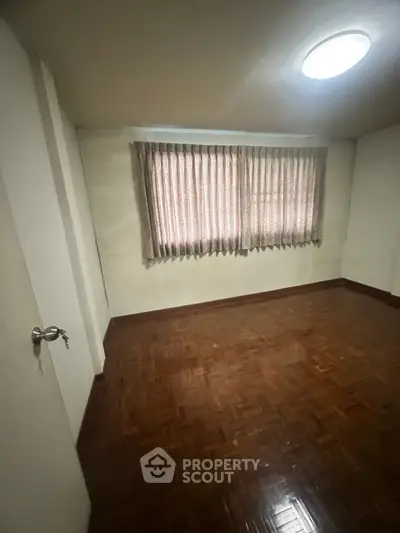 Spacious empty room with wooden flooring and large window, perfect for customization.