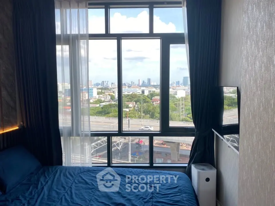 Modern bedroom with large window offering stunning cityscape view, featuring cozy blue bedding and elegant curtains.